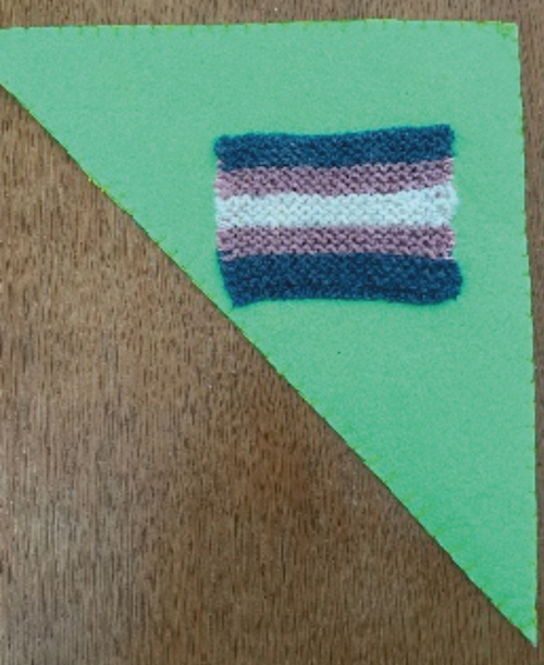 An image of a felt triangle with a knitted trans flag attached
